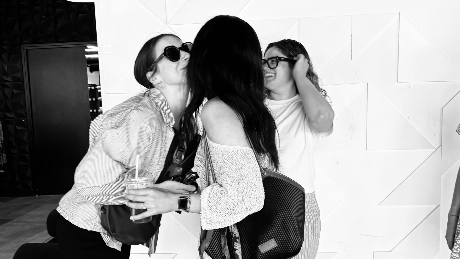 Trois amies partagent une accolade complice, portrait en noir et blanc.