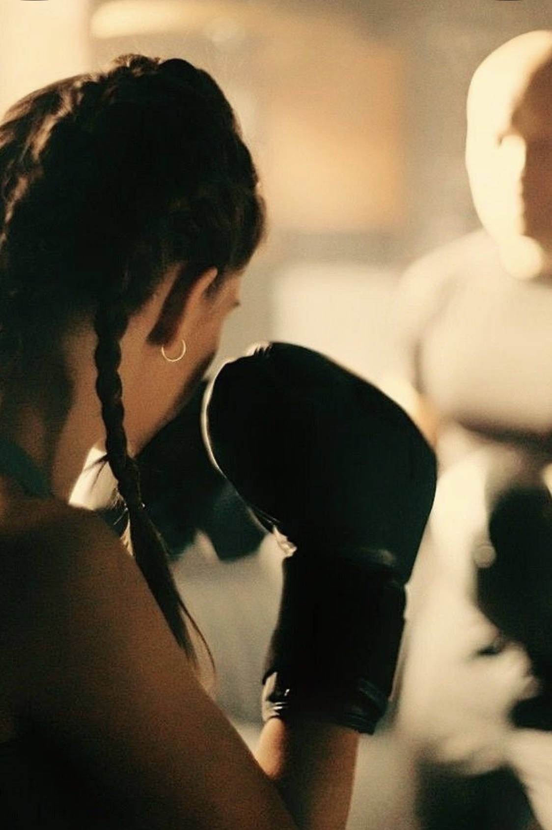A woman with braids, boxing gloves raised in front of her coach, in warm light